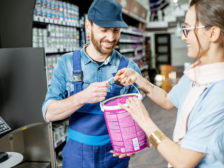 Workman giving bucket with paint to a young woman client in the building shop